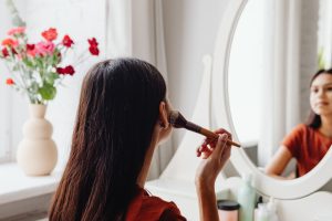 Kobieta nakłada makijaż pędzlem przed lustrem w pomieszczeniu